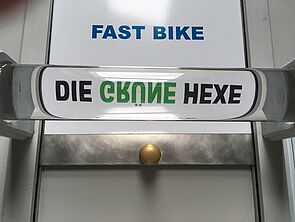 Eine Linse. Darin steht: "Die grüne Hexe". Das Wort "grün" steht auf dem Kopf.