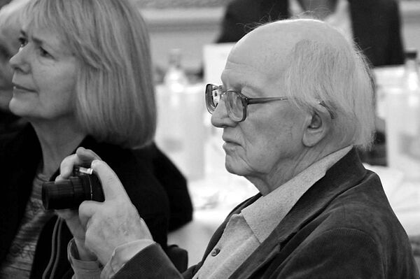 Hans Pölkow sitzt auf einem Stuhl und hält eine Fotokamera in der Hand.