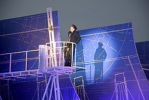 Ein Mann steht auf einem Podest in blauem Licht. 