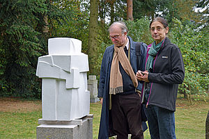 Ein Mann und eine Frau stehen in einem Garten und betrachten eine Skulptur.