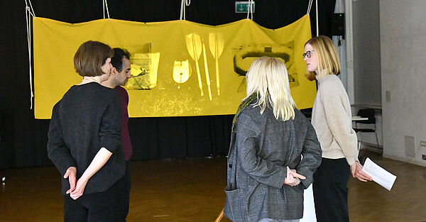 Menschen stehen vor einer gelben Leinwand.