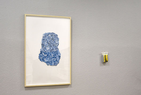 Ein blaues Papier gerahmt hängt an der Wand. Rechts daneben eine gefaltete Rettungsdecke in einer kleinen Tüte. 
