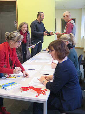 An einem langen Tisch sitzen Frauen und Männer. Sie begrüßen die Gäste und haken ihre Namen auf der Teilnehmerliste ab. 