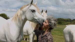 Eine Frau hält ihren Kopf an ein weißes Pferd.
