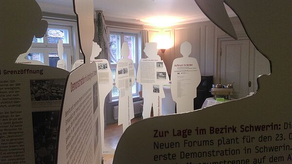 Weiße Pappaufsteller haben die Silhouette von Frauen und Männern. Die Aufsteller sind mit Informationen und Bildern bedruckt.