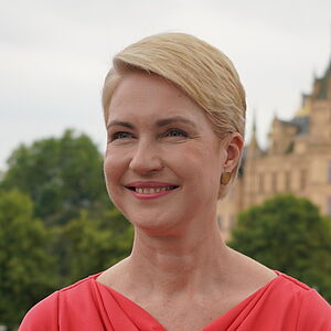 Manuela Schwesig steht in einem roten Kleid auf der Straße. Im Hintergrund das Schweriner Schloss.