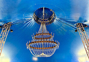 Ein Kronleuchter. Er hängt an einer blauen Decke. 