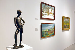 Ein Büste zeigt einen Jungen. Rechts hängen drei Bilder an der Wand.