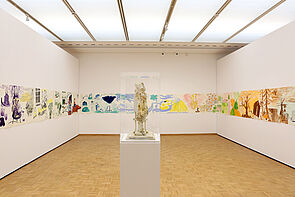 Ein Kunstobjekt steht in der Mitte des Raumes. An den Wänden hängen Bilder.