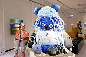 Ein Mann und eine blau-weiße Figur. Zwei Kunstobjekte aus der Ausstellung.