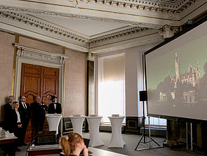 Auf einer Leinwand wird das Filmprojekt vorgestellt. Zu sehen ist das Schweriner Schloss.