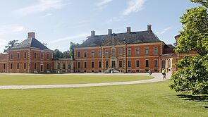 Wiese und ein Baum. Im Hintergrund steht ein historisches Gebäude.