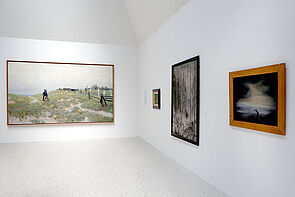 Bilder hängen an der Wand. Das große Bild zeigt eine Landschaft.