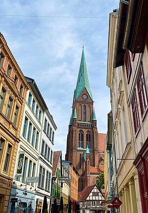 Links und rechts stehen historische Gebäude aus der Innenstadt. Dazwischen ragt im Hintergrund der Dom empor.