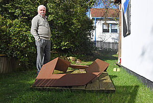 Helmut Senf steht im Garten vor einer Bodenskulptur.