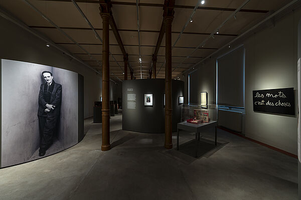 Ein nur leicht beleuchteter Ausstellungsraum. An den Wänden hängt moderne Kunst.