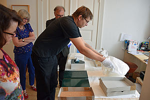 Dr. Christian Frosch öffnet Kartons mit seiner Kunst. Um ihn herum stehen zwei Frauen und ein Mann.