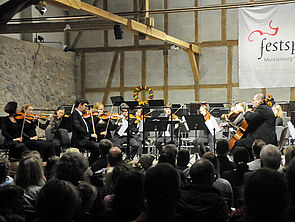 Ein Raum voller Zuschauerinnen und Zuschauer. Vor ihnen spielt ein Orchester.