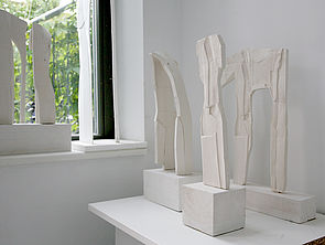 Drei weiße Skulpturen auf weißen Sockeln.