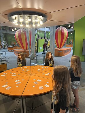 Kinder stehen um einen runden, orangenen Experimentiertisch herum. 