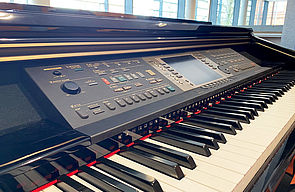 Ein Klavier in Nahaufnahme mit Blick auf die Tasten und das Klavierpult mit vielen Knöpfen, zum Beispiel zum Navigieren und Pausieren.