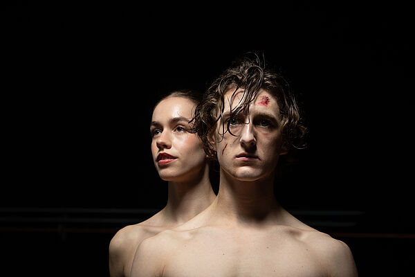 Eine Frau und ein Mann. Zwei Tänzer. Sie stehen ausgeleuchtet im dunklen Raum.