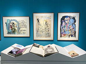 Auf einem Tisch liegen Bücher von Armin Mueller-Stahl. An der Wand hängen drei Bilder.