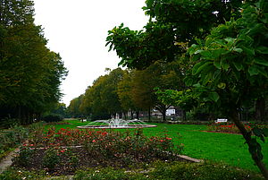 Ein Park mit Blumen, Bäumen und einer Wasserfontäne.