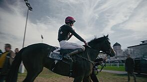Ein Jockey auf einem Pferd. Im Hintergrund ein Schloss.