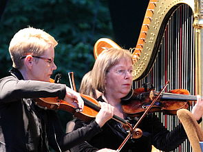 Zwei Geigerinnen neben einer Harfe.