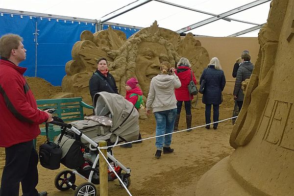 Menschen gehen an den Sandskulpturen vorbei.