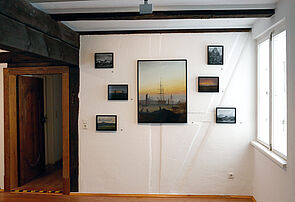 Sechs kleine und ein großes Bild hängen an der Wand.