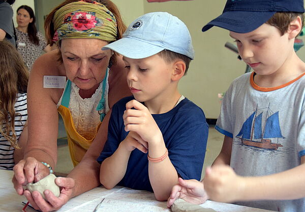 Marion Neumann steht neben zwei Kindern und hat Ton in der Hand.