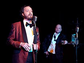 Zwei Musiker auf der Bühne. Einer singt ins Mikrofon.