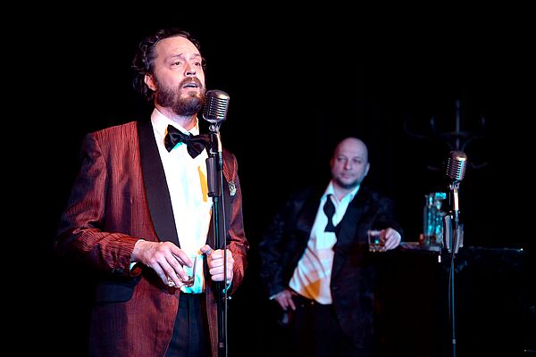 Zwei Musiker auf der Bühne. Einer singt ins Mikrofon.