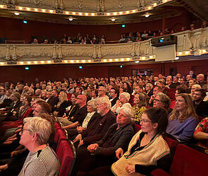 Ein Theatersaal. Darin sitzen viele Menschen. 