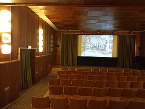 Blick in einen leeren Kinosaal. Auf der Leinwand läuft ein Film.