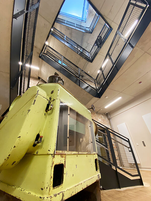 Im Foyer steht eine gelbe, etwa mannshohe Mühle. Die Farbe ist an vielen Stellen schon abgeblättert. Das Treppenhaus reicht fünf Stockwerke nach oben. An den Treppen befinden sich schwarzbraune Eisengeländer.