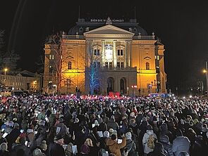 Ein Platz voller Menschen. Sie singen Weihnachtslieder.