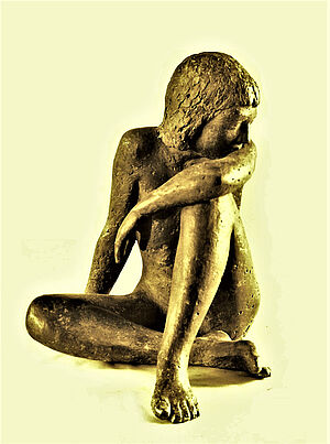 Eine Figur aus Bronze. Zu sehen ist eine junge Person, die sitzt. Ein Bein ist angewinkelt.