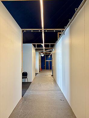 Ein schmaler Flur. Links und rechts stehen Wände. 