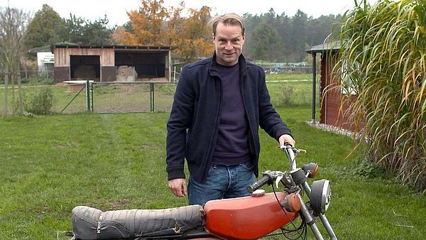 Hinnerk Schönemann steht auf einer Wiese an einem Moped.