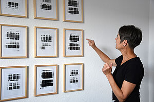 Iris vom Stein steht vor ihren Fotos. Sie zeigt auf ein Bild.