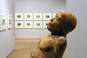 Eine Büste in der Ausstellung. Im Hintergrund sind Bilder zu sehen.