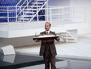 Schauspieler Max Niemeyer steht an Deck und hält ein Modell der Titanic in der Hand.
