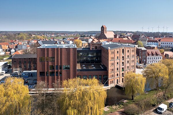 Die Kulturmühle steht mit der rückseitigen Fassade wie ein H am Ufer der Elde. Im Hintergrund erheben sich die Dächer der Altstadt. 