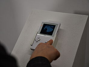 Ein Finger drückt auf die Taste eines Gameboys.