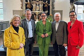 Fünf Personen - drei Frauen, zwei Männern - stehen nebeneinander in einer Kirche. 