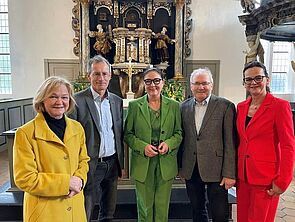Fünf Personen - drei Frauen, zwei Männern - stehen nebeneinander in einer Kirche. 