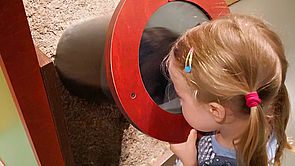 Ein Mädchen schaut durch ein Guckloch.